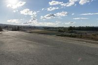 a empty asphalt road with a hill in the background under a cloudy blue sky and sun