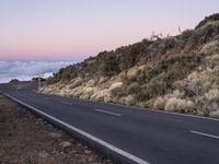 an empty winding road on a mountain with the sun set above the mountains in the background