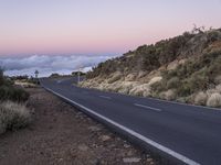 an empty winding road on a mountain with the sun set above the mountains in the background