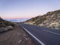 an empty winding road on a mountain with the sun set above the mountains in the background