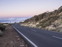 an empty winding road on a mountain with the sun set above the mountains in the background