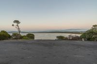 an empty asphalt road with trees on top at the lake's edge and a beautiful sky