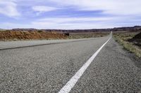 a motorcycle is on the empty asphalt road between two hills and a road side with a bull in it