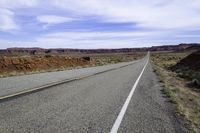 a motorcycle is on the empty asphalt road between two hills and a road side with a bull in it