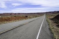 a motorcycle is on the empty asphalt road between two hills and a road side with a bull in it