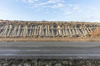 an empty asphalt road near an overhangped rock wall near the highway surface, under a blue sky