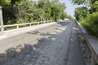 an empty, asphalt street with a bridge and green trees to the side of each road