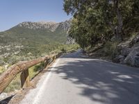 an empty asphalt street with a wooden fence next to a mountain top as the sun shines on it