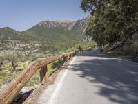 an empty asphalt street with a wooden fence next to a mountain top as the sun shines on it