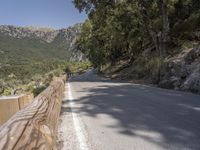 an empty asphalt street with a wooden fence next to a mountain top as the sun shines on it