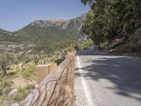 an empty asphalt street with a wooden fence next to a mountain top as the sun shines on it