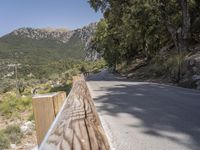 an empty asphalt street with a wooden fence next to a mountain top as the sun shines on it