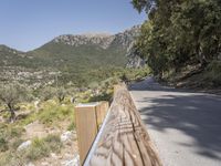 an empty asphalt street with a wooden fence next to a mountain top as the sun shines on it