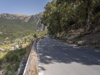 an empty asphalt street with a wooden fence next to a mountain top as the sun shines on it