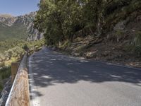 an empty asphalt street with a wooden fence next to a mountain top as the sun shines on it