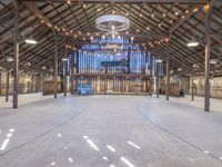 an empty barn with wood and string lights in the ceiling of it, and a stage in the center that's ready to be used for the stage