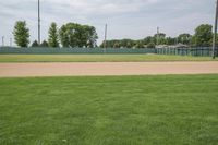 a baseball field that is empty in a field near trees and buildings on a grassy green field