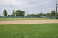 a baseball field that is empty in a field near trees and buildings on a grassy green field