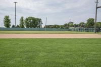 a baseball field that is empty in a field near trees and buildings on a grassy green field