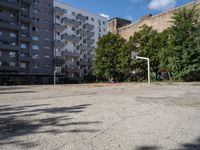 an empty basketball court is seen in this photograph from the corner in front of an apartment complex