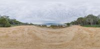 an empty beach near a wide body of water and trees and clouds in the air