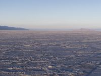 there is a picture taken from the airplane of an empty beach covered in ice with mountains in the distance