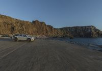 an empty beach sits in front of some rocks near the ocean as the moon goes down