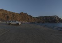 an empty beach sits in front of some rocks near the ocean as the moon goes down