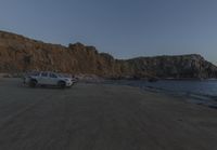 an empty beach sits in front of some rocks near the ocean as the moon goes down