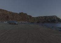 an empty beach sits in front of some rocks near the ocean as the moon goes down