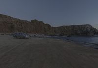 an empty beach sits in front of some rocks near the ocean as the moon goes down