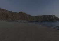 an empty beach sits in front of some rocks near the ocean as the moon goes down