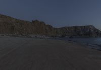 an empty beach sits in front of some rocks near the ocean as the moon goes down