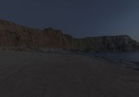 an empty beach sits in front of some rocks near the ocean as the moon goes down