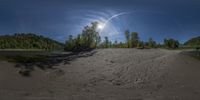 a fish eye shot of an empty beach and forest area with a bridge on the shoreline