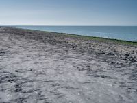 a long empty beach that is near a body of water on a sunny day with clear skies