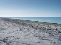 a long empty beach that is near a body of water on a sunny day with clear skies