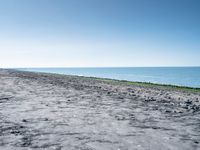 a long empty beach that is near a body of water on a sunny day with clear skies