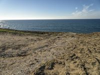 a beach is empty with rocks and some water and birds flying above it on a clear, sunny day