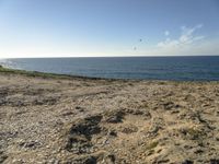 a beach is empty with rocks and some water and birds flying above it on a clear, sunny day