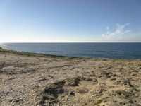 a beach is empty with rocks and some water and birds flying above it on a clear, sunny day