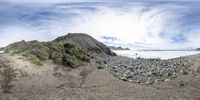 a fisheye lens photo of an empty beach with rocks, grass, and waves