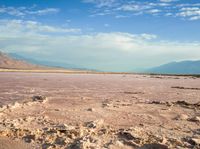 an empty beach is covered in some pink water and some sand near mountains with clouds