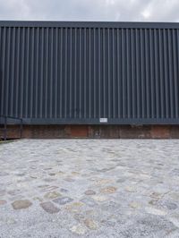 an empty bench sitting on top of a brick pavement in front of a black wall