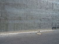 an empty bench outside of a concrete building with a red brick walkway behind it and a gray wall