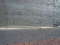 an empty bench outside of a concrete building with a red brick walkway behind it and a gray wall