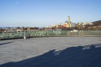 some benches are empty on the concrete patio near a fence and large city skyline in the background