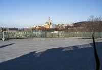 some benches are empty on the concrete patio near a fence and large city skyline in the background