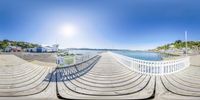 360 - viewing of an empty boardwalk near water on sunny day with clouds overhead and boats anchored nearby