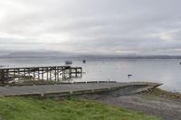 a pier sits empty on a cloudy day, overlooking the water with boats out to sea